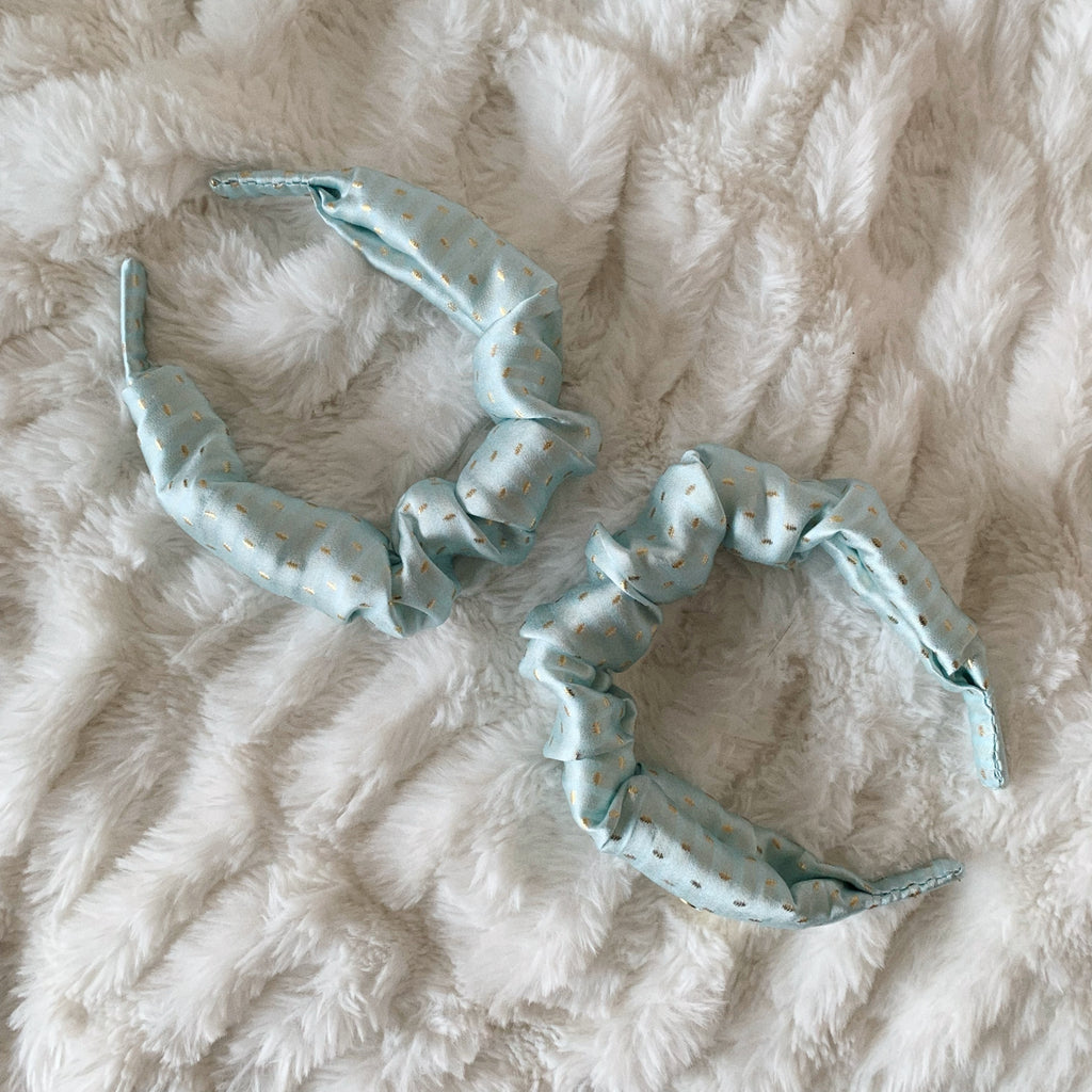Flat lay of baby blue silk scrunchie headband with gold spots.