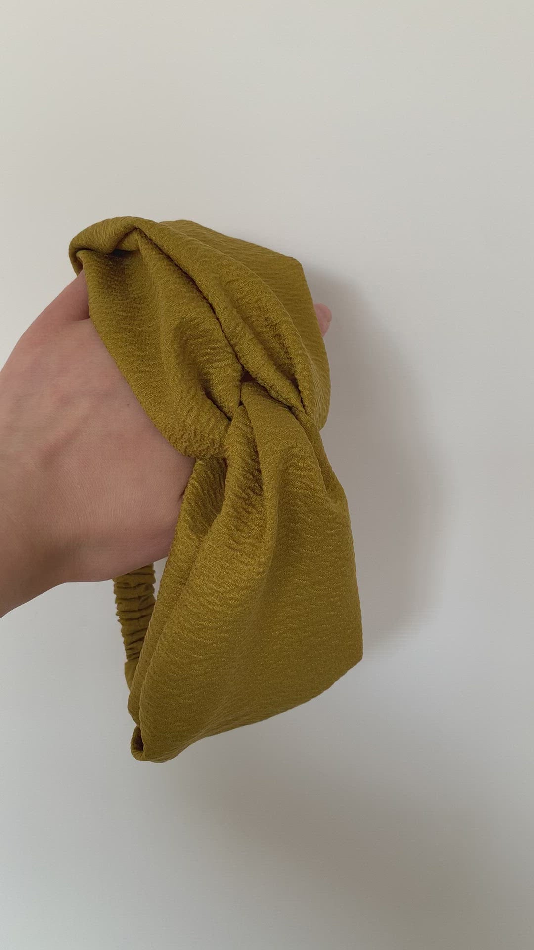 Video of a model's hand holding a twisted headband in Chartreuse.