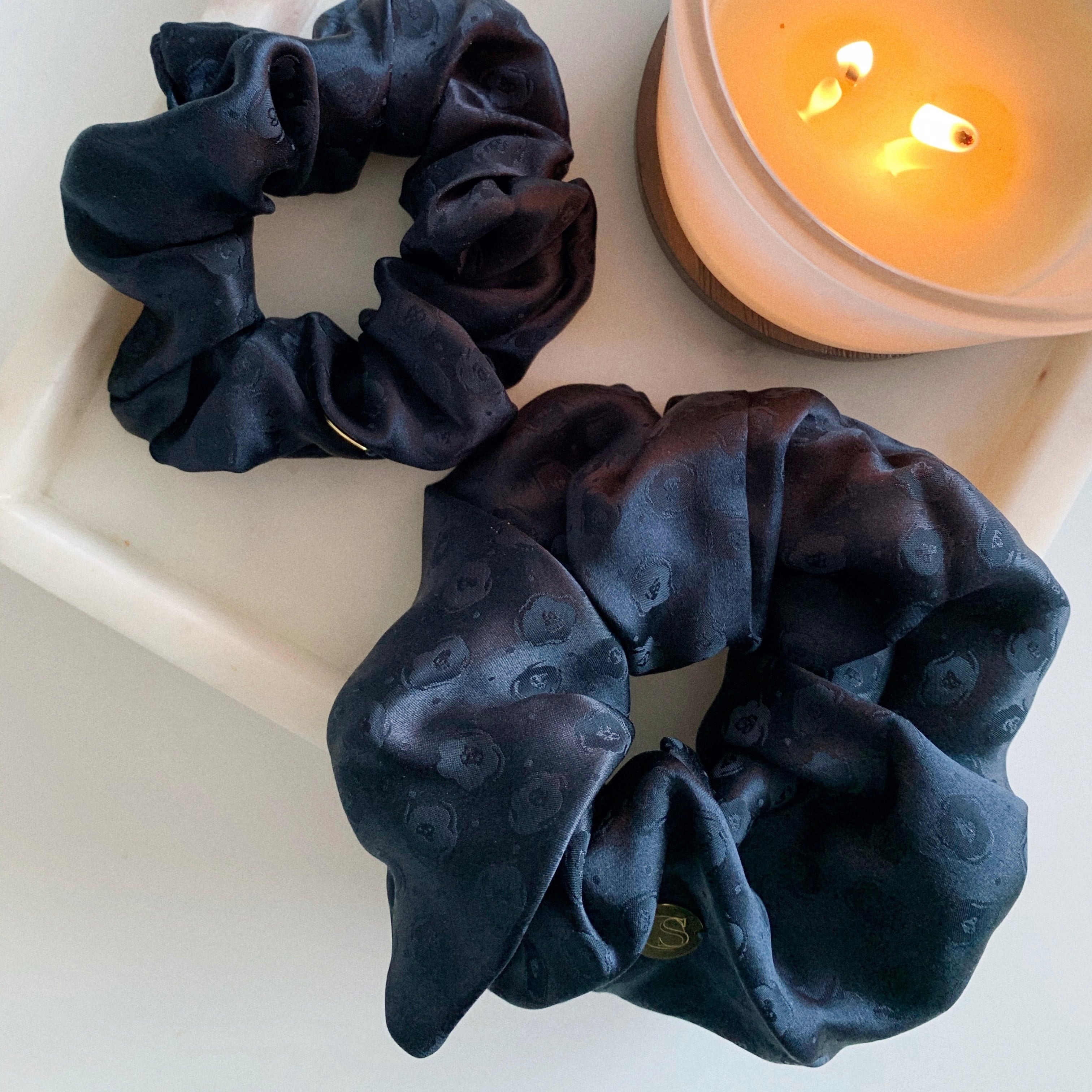 Sapphire - Flat lay of one jumbo size scrunchie and one standard size scrunchie in a inky blue silk satin jacquard.