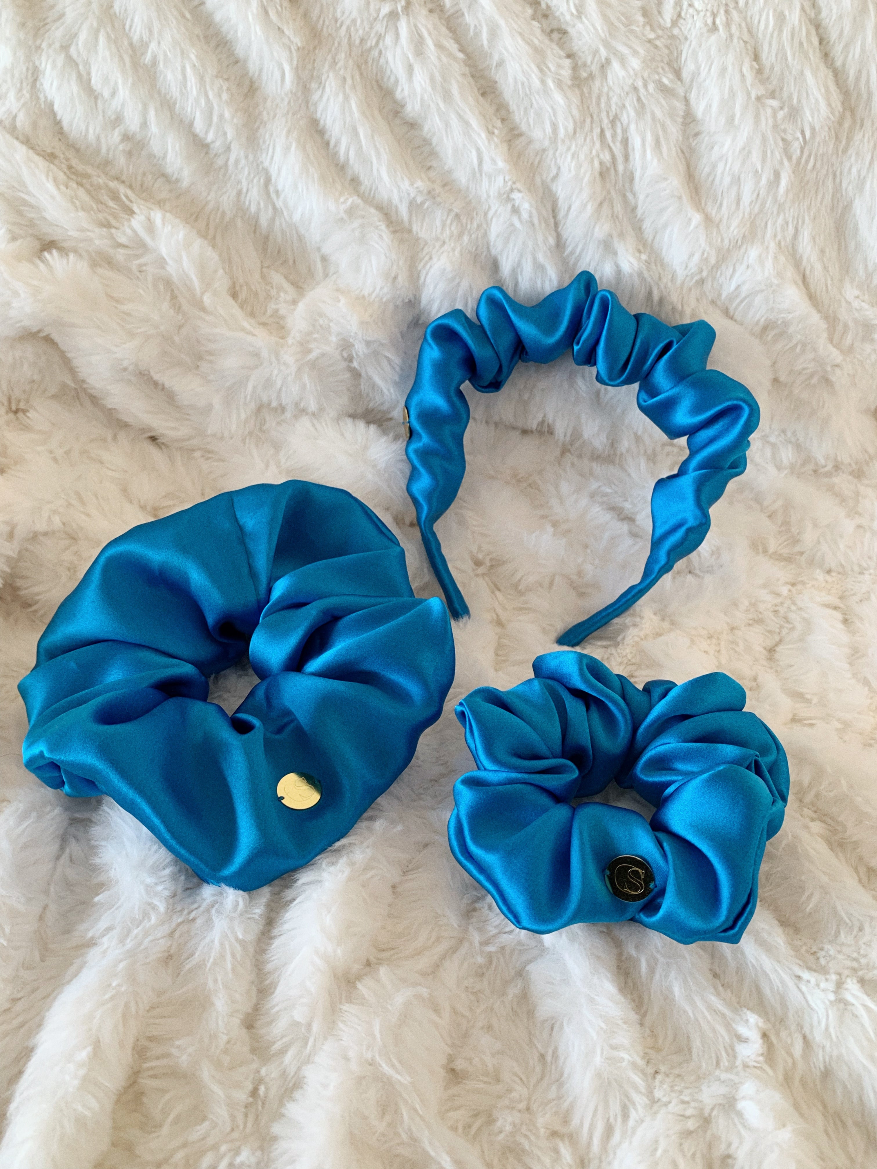 Flat lay of one standard size scrunchie, one jumbo size scrunchie and one scrunchie headband in blue.