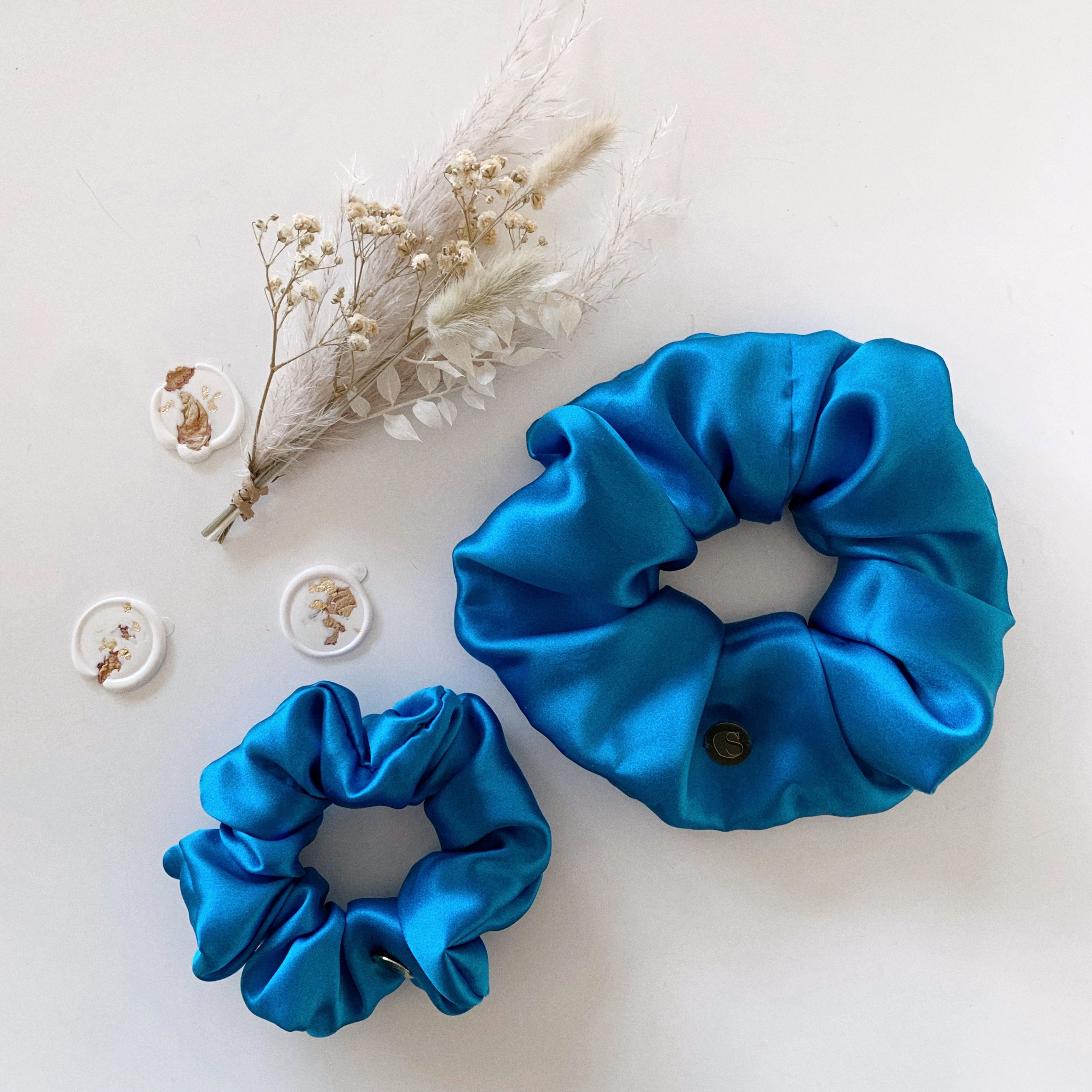 Flat lay of one standard size scrunchie and one jumbo size scrunchie in blue.