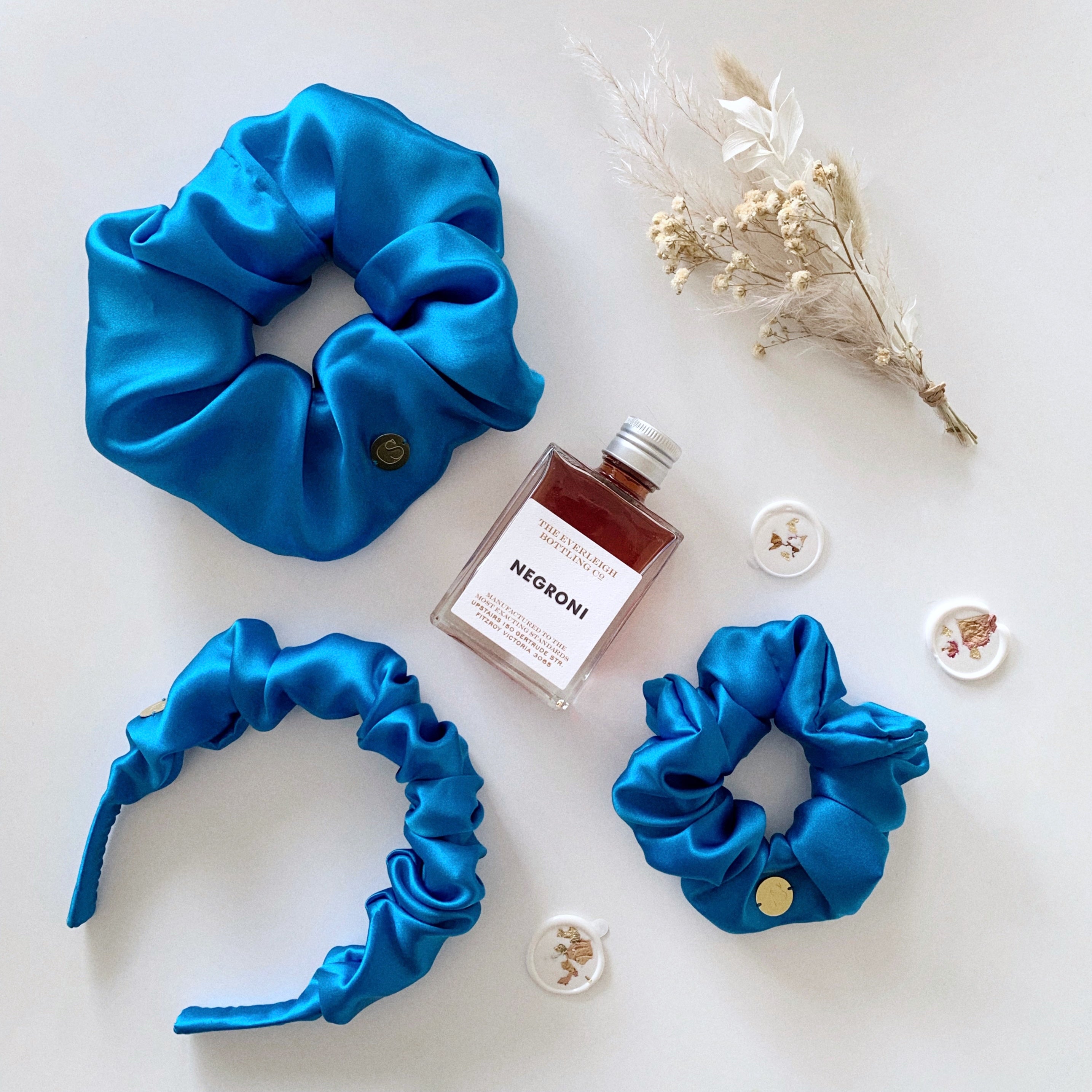 Flat lay of one standard size scrunchie, one jumbo size scrunchie and one scrunchie headband in blue.