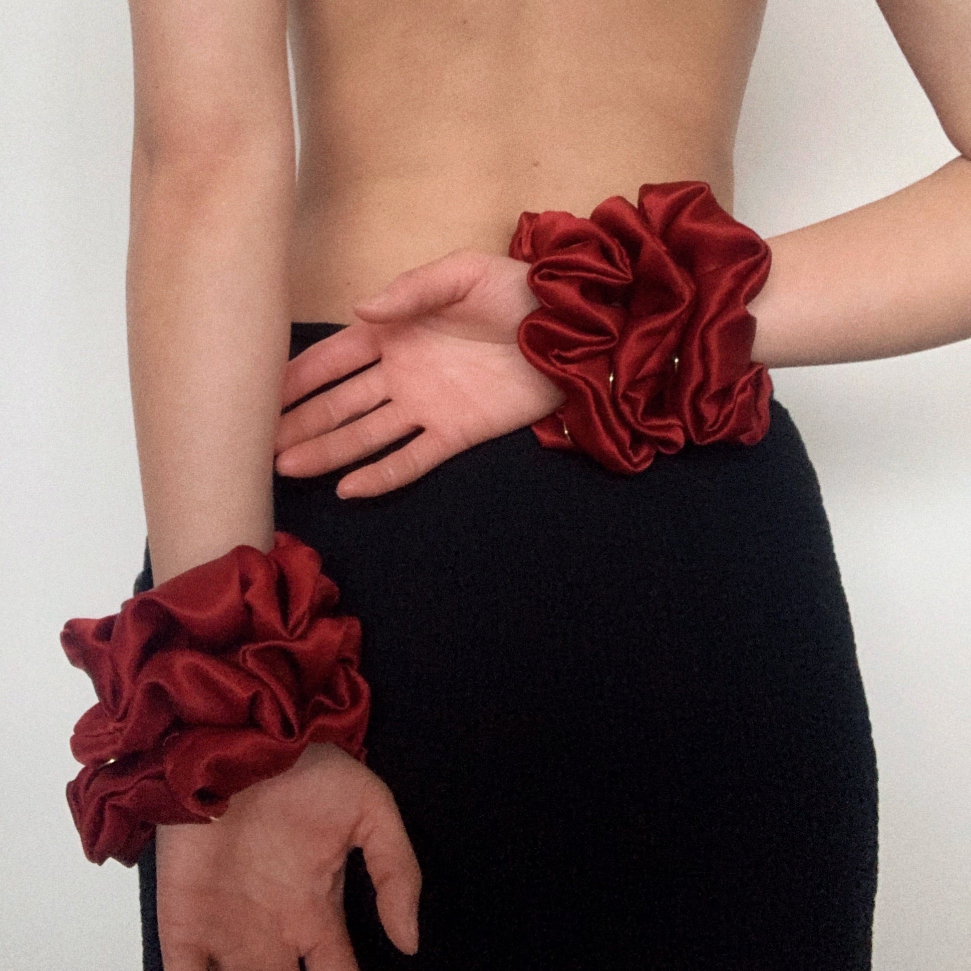 Model wearing deep red silk satin scrunchies on wrists.