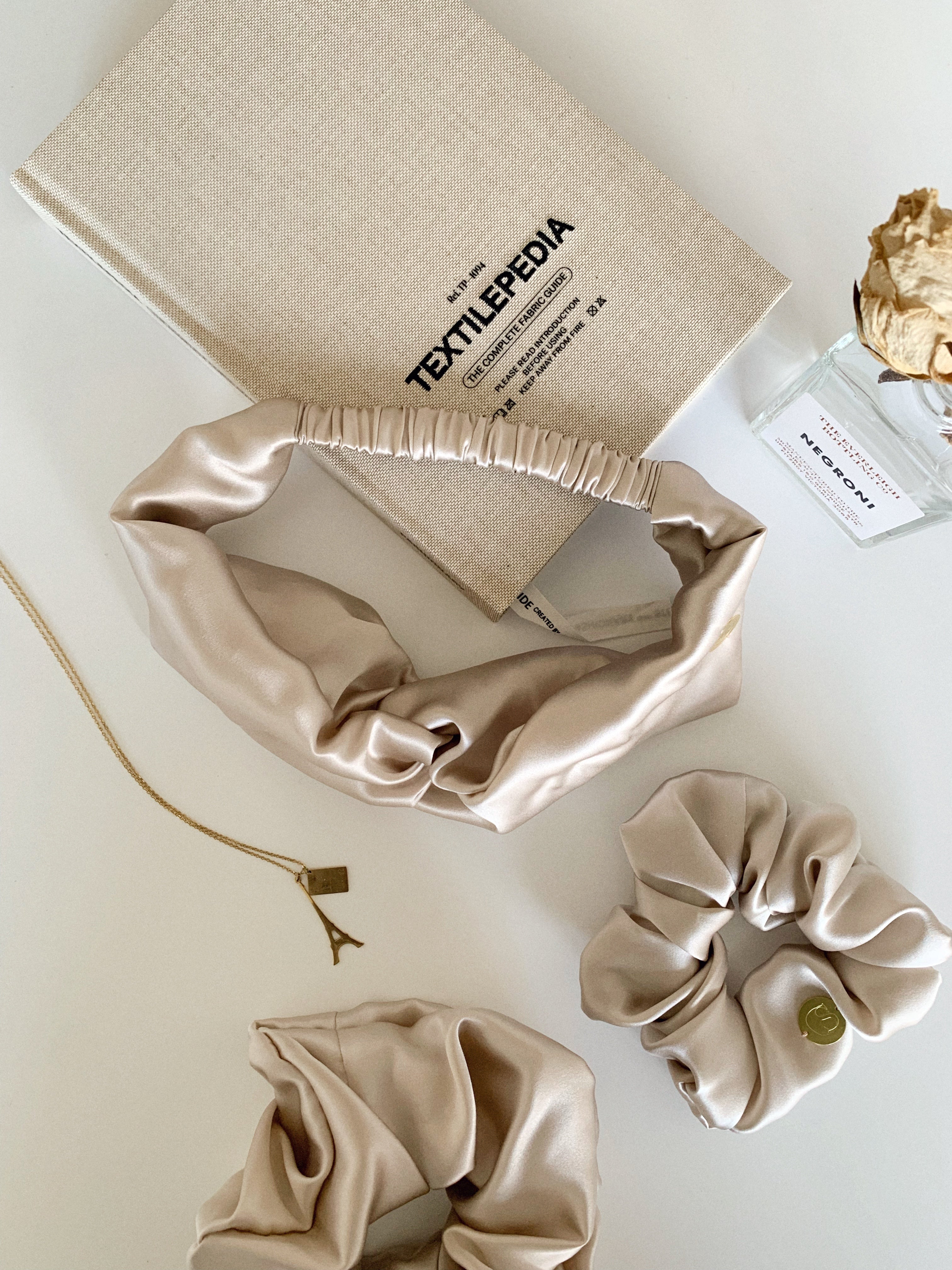 Flat lay of a headband, standard scrunchie and large scrunchie in nude silk satin.
