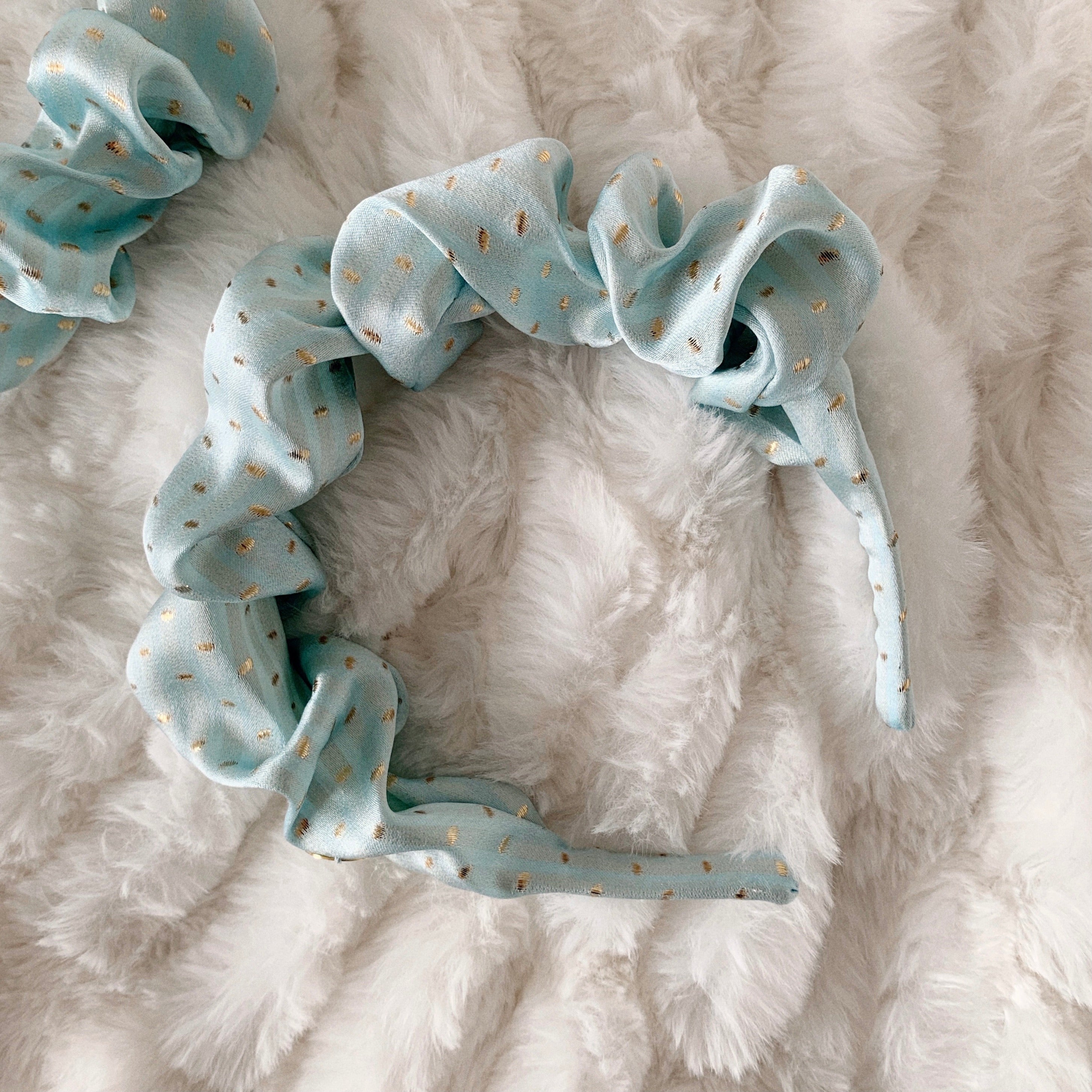 Flat lay of baby blue silk scrunchie headband with gold spots.